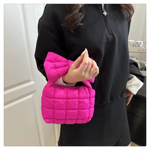 Close-up of fuchsia quilted handbag featuring a large puffy bow handle and grid stitching