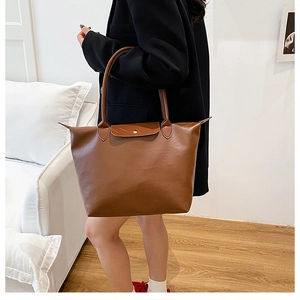 Detail view of large brown leather tote bag with flap closure on model in black blazer