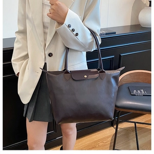 Detail of dark brown leather tote bag showing handle, flap cover and metal snap closure
