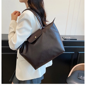 Detail of a large capacity brown leather tote bag with classic snap-button flap and handle