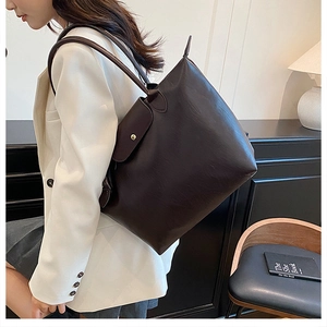 Close-up of a large dark brown faux leather tote bag worn by a model in white suit