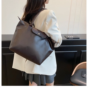 Detail of a large dark brown faux leather tote bag with flap closure and gold snap button
