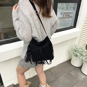 Chic black fringe underarm bag with long tassels shown on shoulder in urban street style