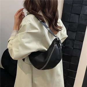 Minimalist black crescent shoulder bag with silver chain detail on beige coat