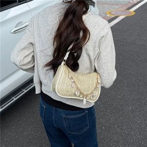 Straw baguette bag with gold chain and sea shell charms shown in a lifestyle street view