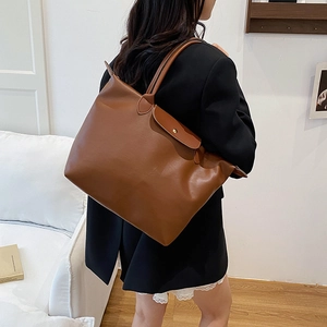 Brown leather large capacity tote bag with gold snap button worn by a model in a room