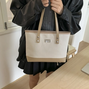 Minimalist beige woven tote bag with khaki leather handles and silver metal accents