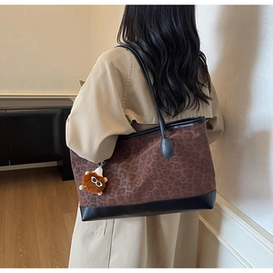 Detail of leopard print tote bag with plush charm accessory on a model shoulder