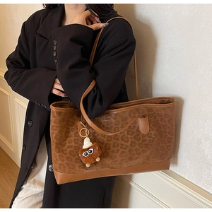 Detail of leopard print tote bag featuring brown leather trim and a plush eye charm