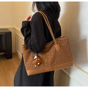 Shoulder shot of large leopard print tote bag with brown leather trim and plush charm