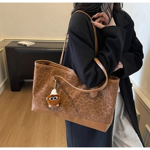 Detail of leopard print tote bag with brown leather trim and cute plush bear charm