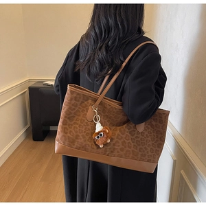 Close-up of leopard print suede tote with brown leather straps and a plush doll charm