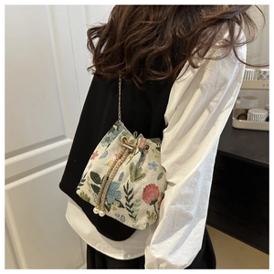 Close-up of vintage floral embroidered bucket bag with pearl drawstring and gold chain strap
