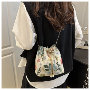 Ethnic embroidered bucket bag with floral patterns and pearl drawstring on a female model