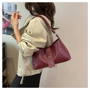 Detail of burgundy leather shoulder bag with gold metal eyelets shown on a model