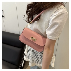 Pink minimalist crossbody bag with gold buckle hardware worn by model in a home setting
