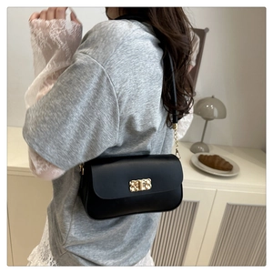 Detail of elegant black shoulder bag with gold woven texture metal buckle and chain strap