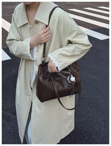 Detail of dark brown tote bag with fashion tag and baseball charm on beige trench coat
