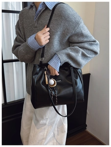 Detail of black leather tote bag with fashion label and baseball keychain accessory