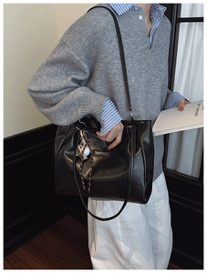 Close-up of black leather tote bag with fashion tag and baseball charm on model