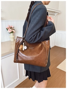 Detail of a large brown faux leather tote bag with creative teddy bear and baseball charms