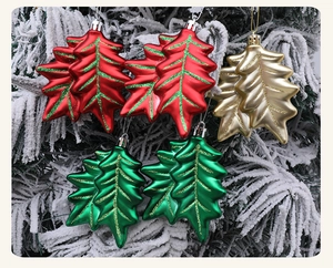 Detail of red, green and gold leaf Christmas ornaments with glitter veins on snowy branches