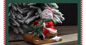 Festive ceramic snowman ornament on a wooden sleigh with pine needles for holiday decor