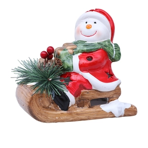 Close-up of ceramic Christmas snowman on a wooden sleigh with pine and red berry accents