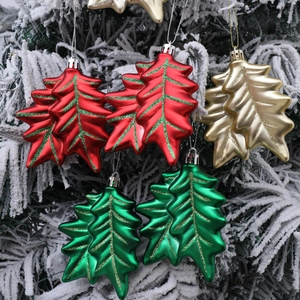 Glittery holly leaf Christmas ornaments in red, gold, and green on a snowy tree branch