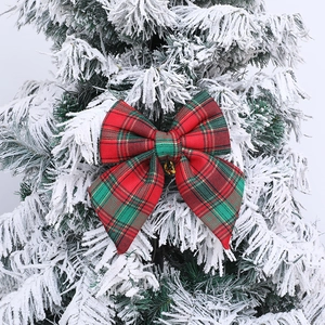 Red and green plaid Christmas bow ornament hanging on a snowy Christmas tree branch