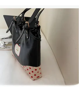 Detail of a black tote bag featuring a red apple print and polka dot bottom pattern