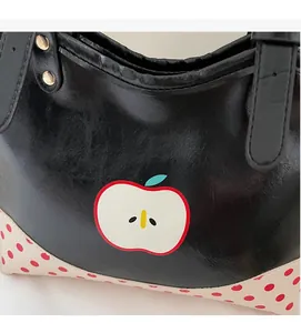 Close-up of black tote bag with white apple print and red polka dot corner details