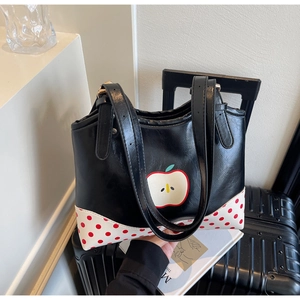 Detail view of the black tote bag with apple print and red polka dot corners on luggage