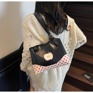 Detail of black tote bag with white apple motif and red polka dot base worn by a model