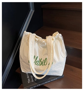 Detail of cream tote bag featuring green script print and textured drawstring closure