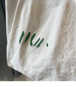 Detail of white wrinkled fabric tote with green text and soft texture for daily use