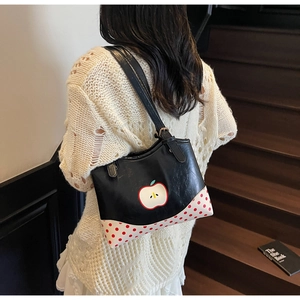 Detail of a chic black shoulder bag with apple motif and red polka dots worn by a model