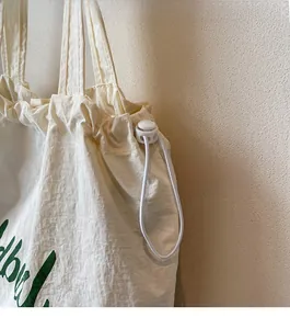 Detail of white drawstring bucket bag showing the functional plastic toggle closure