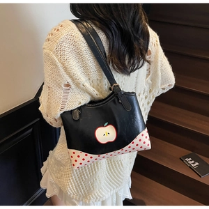 Detail of a black tote bag with red apple print and polka dot accents on wooden stairs