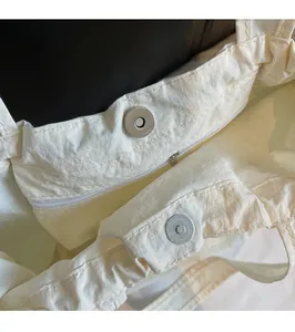 Detail view of the magnetic snap closure and internal zipper pocket of the off-white tote bag