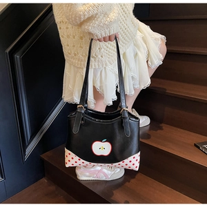Detail view of black PU tote bag with apple print and red polka dot accents held by model