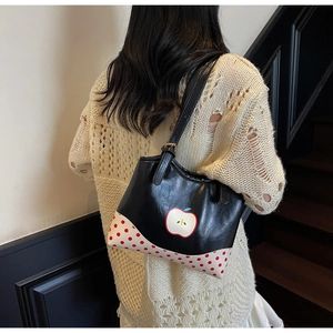 Detail of black glossy apple pattern tote bag with red polka dot corner patch on shoulder