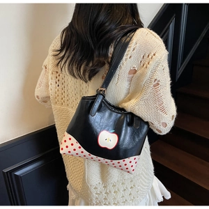 Detail view of the white apple print and red polka dot corners on the black tote bag