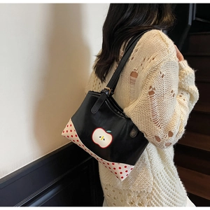 Detail of a black tote bag with red polka dots and apple design worn by a model