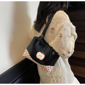 Detail of cute apple polka dot tote bag worn by a model in a beige knitted sweater