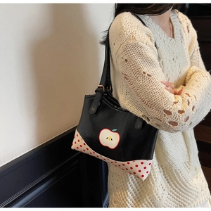 Close-up of a black tote bag featuring a red apple patch and polka dot pattern detail