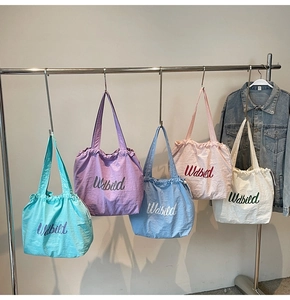 Detail showing colorful drawstring tote bags with embroidered letters hanging on a rack