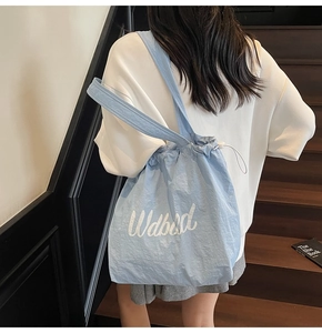 Detail of light blue drawstring tote bag with white lettering on waterproof nylon fabric