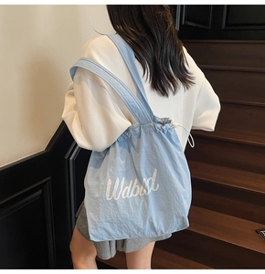 Close-up of light blue drawstring tote bag with letter print shown on a model