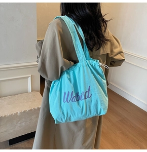 Close-up of bright blue drawstring tote bag with purple logo on light trench coat